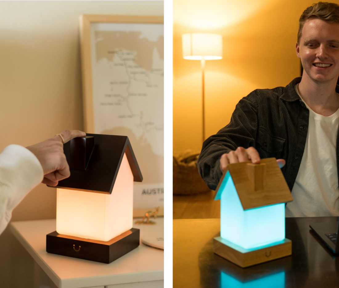 Wooden LuvLink lamp with black roof displayed closed and glowing cyan blue, held open by a person.