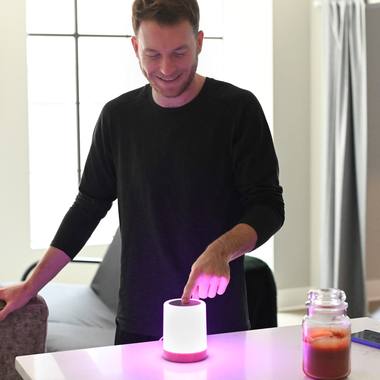 Man smiling while touching a glowing pink LuvLink Friendship Lamp on a table, demonstrating the interactive touch feature.