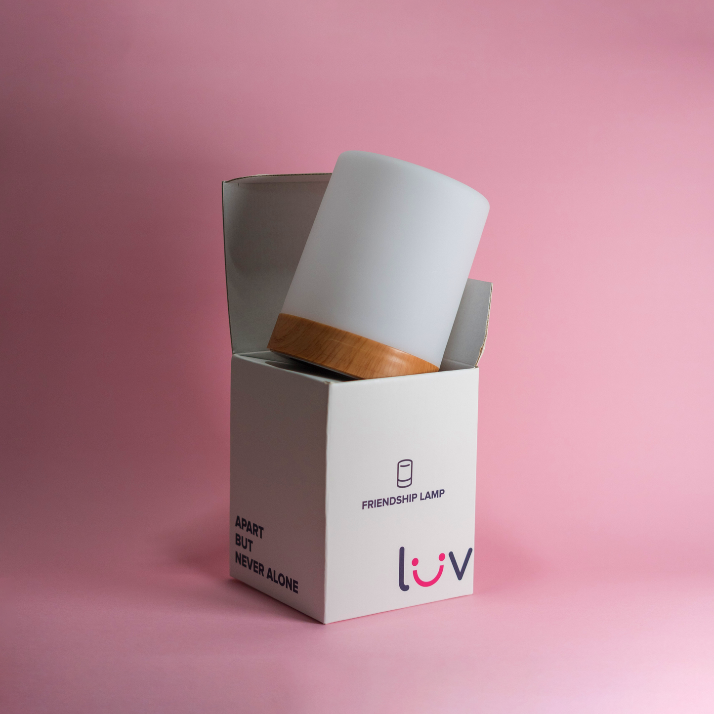 LuvLink Friendship Lamp unboxing showing white cylindrical lamp with wooden base emerging from packaging against pink background.