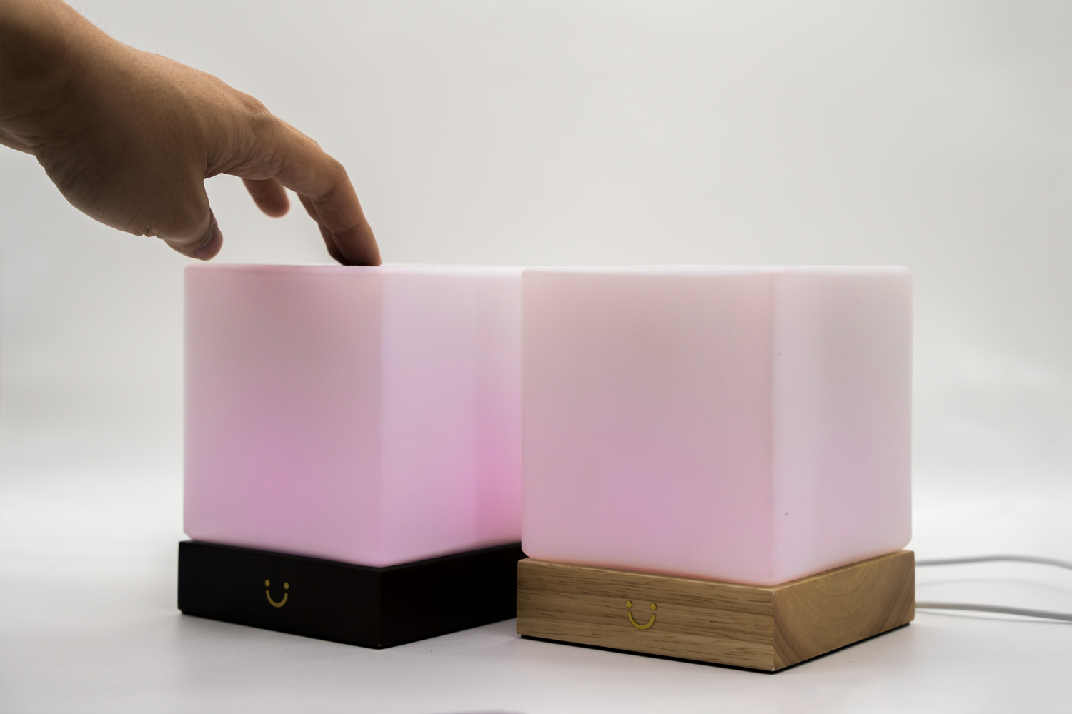 Two pink cube friendship lamps with a hand reaching toward the one with a black base.