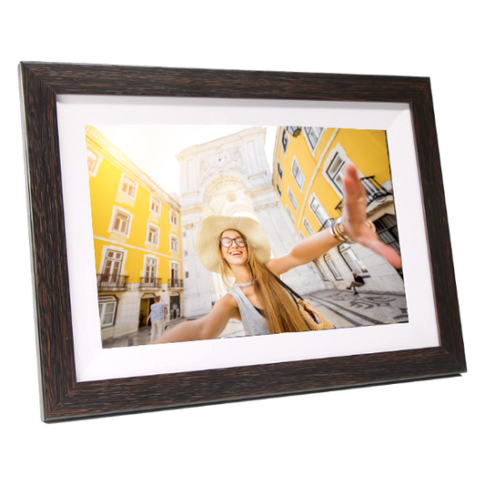 Dark wood digital photo frame displaying a photo of a smiling woman in a yellow hat at a colorful European plaza.